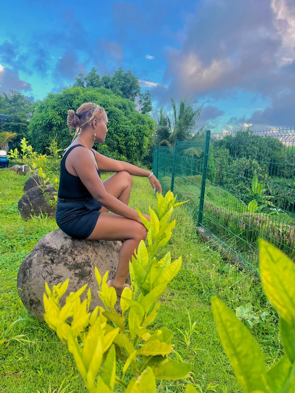 Portrait d'Éline Dracon, thérapeute holistique, assise sur un rocher dans un jardin verdoyant en Guadeloupe.